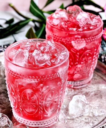 Two icy pink drinks in ornate glassware sit on a silver platter.