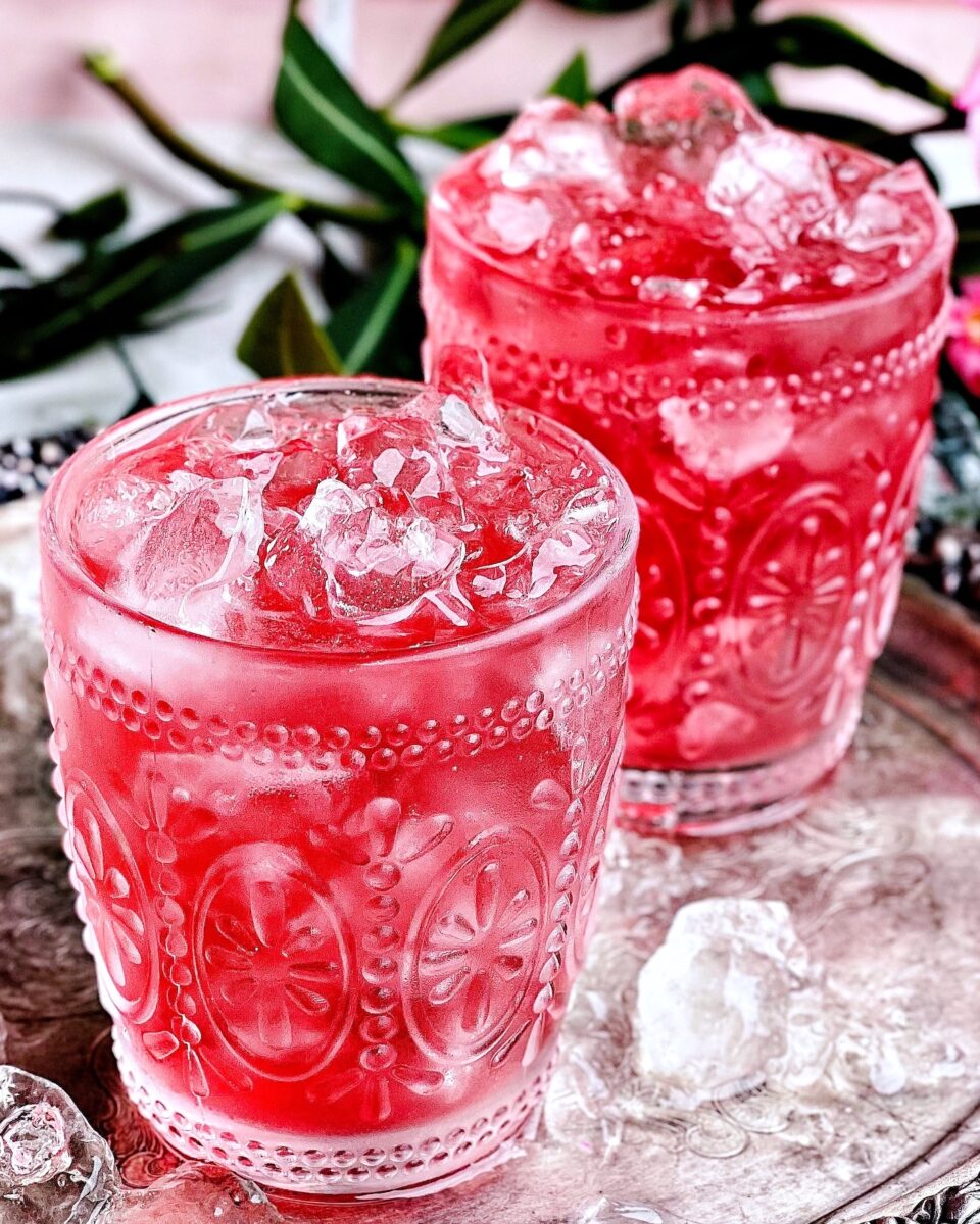 Two icy pink drinks in ornate glassware sit on a silver platter.