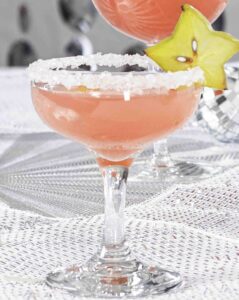 A pink drink in a sugar-rimmed glass, garnished with a slice of starfruit.