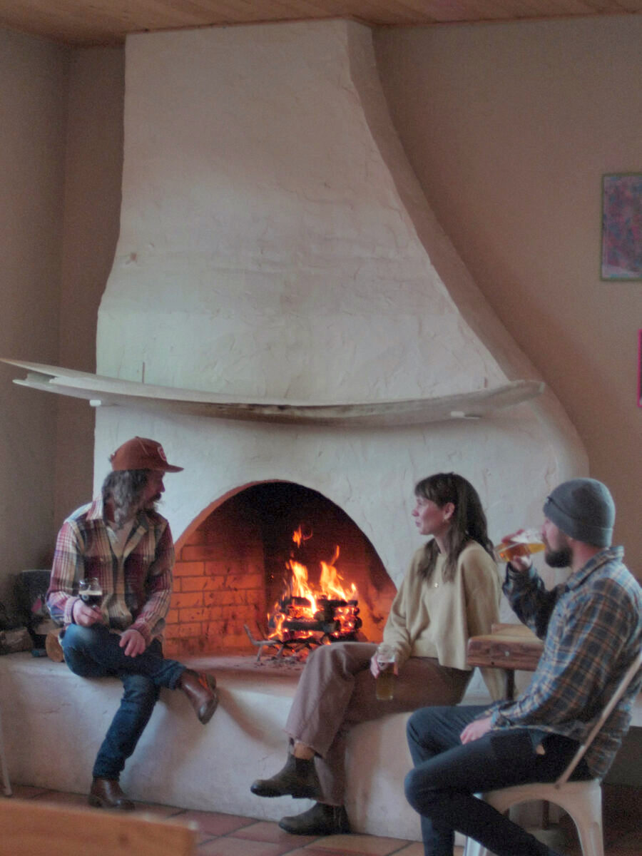 Three people sitting at a white fireplace drinking beer.