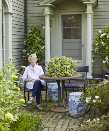 A woman in a button down sits in a garden