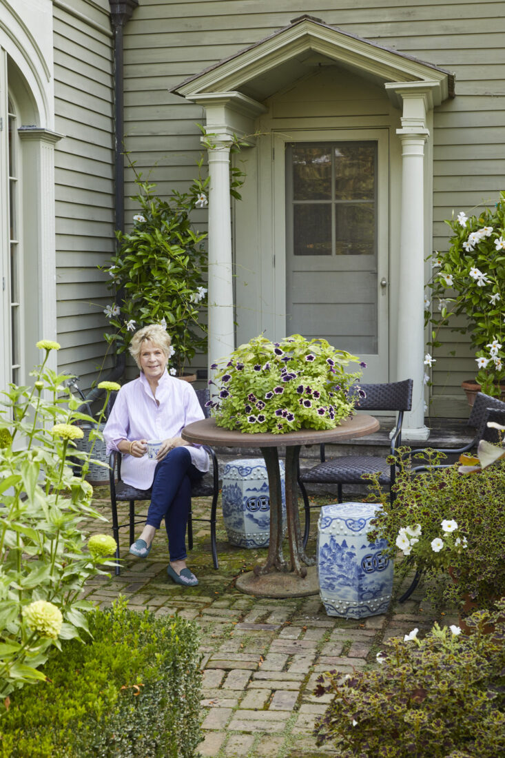 A woman in a button down sits in a garden
