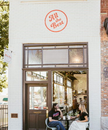 A white brick exterior of a record shop with two people sitting outside at a table