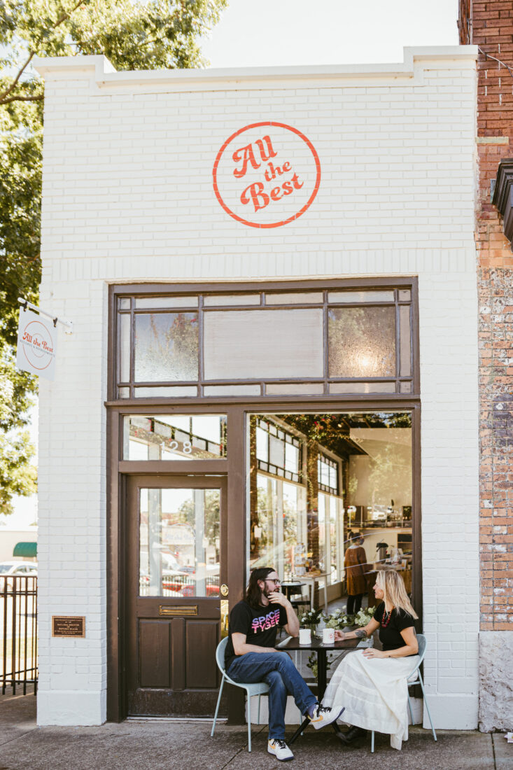 A white brick exterior of a record shop with two people sitting outside at a table