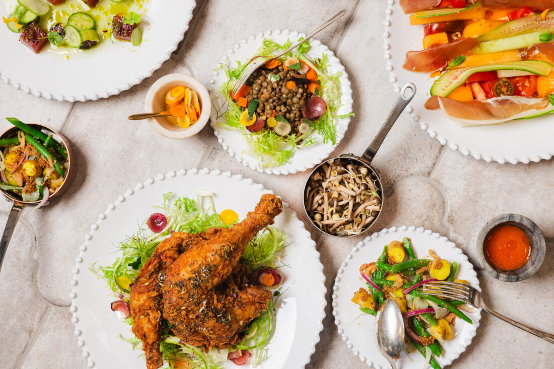 A spread of fried chicken, veggies, salad, and mushrooms on plates against a marble background