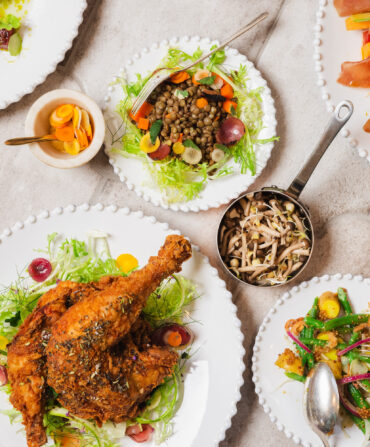 A spread of fried chicken, veggies, salad, and mushrooms on plates against a marble background