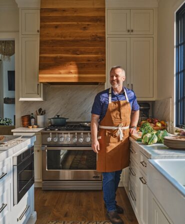 A man in a cooking apron stands in a kitchen and smiles