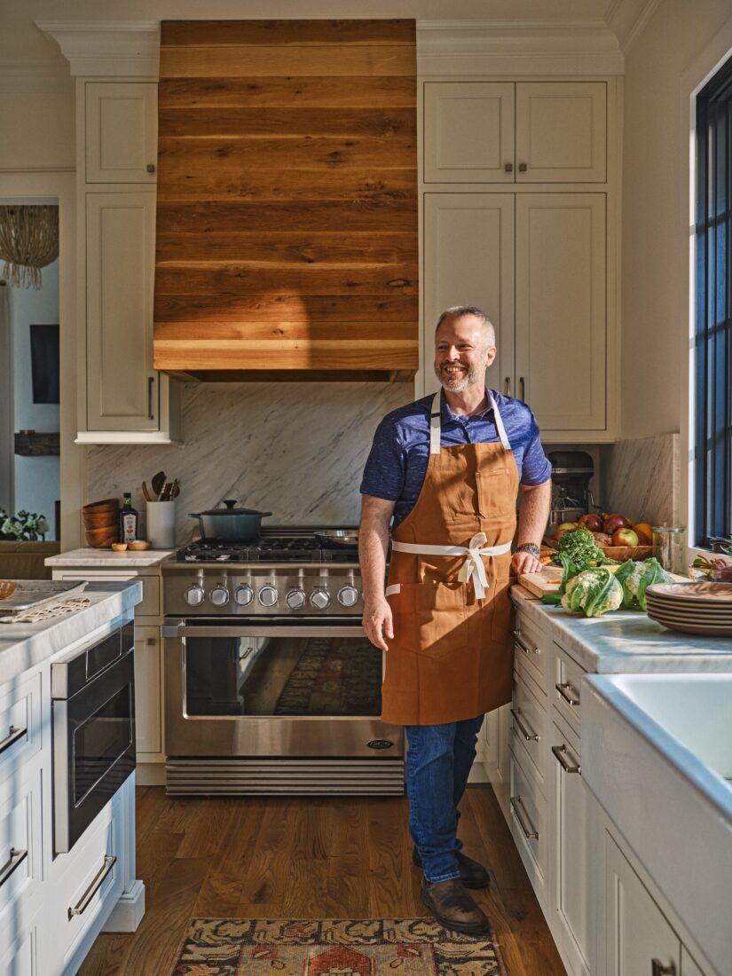 A man in a cooking apron stands in a kitchen and smiles