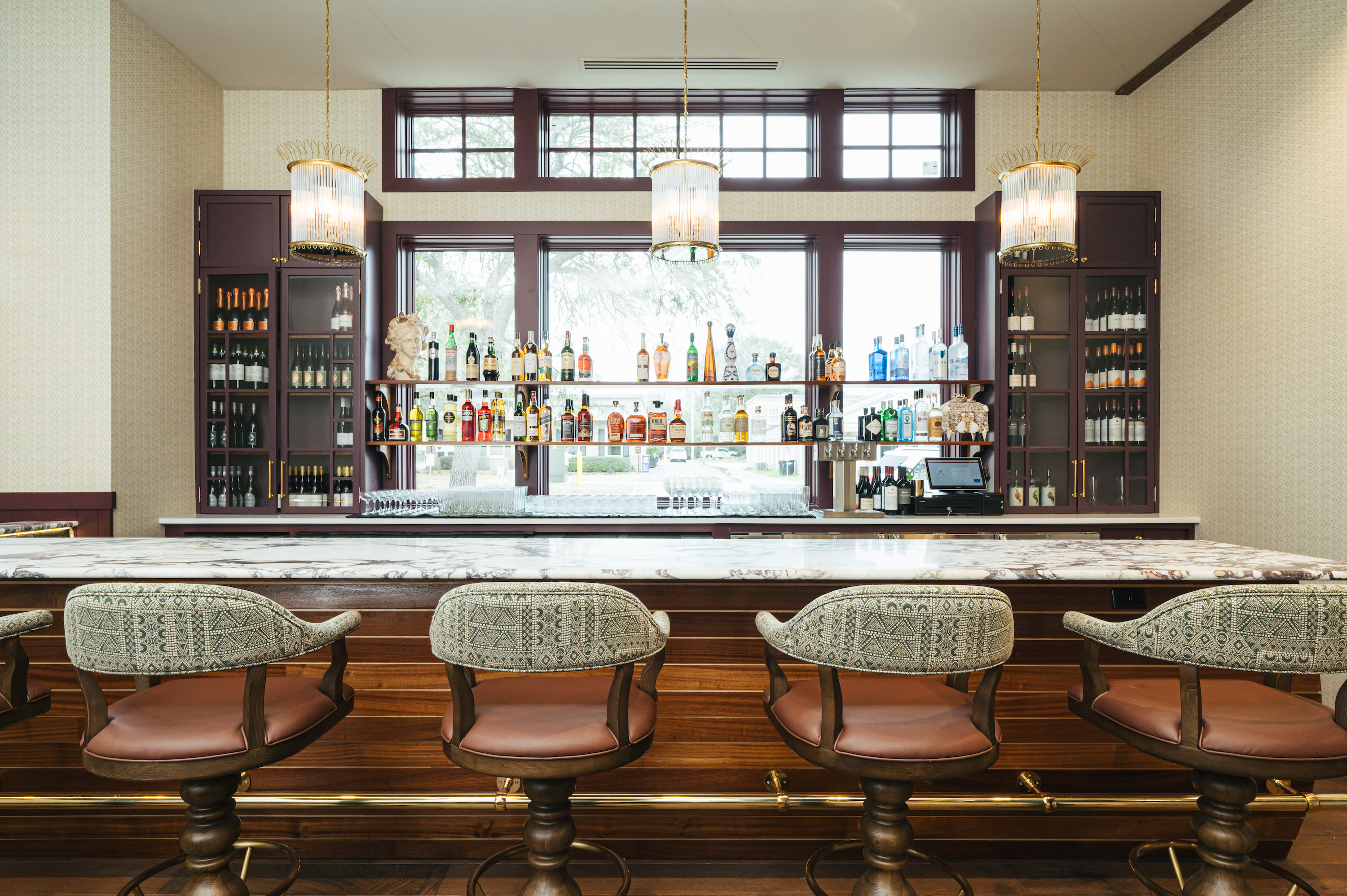 A wood paneled bar with white marble and three glass sconces above.