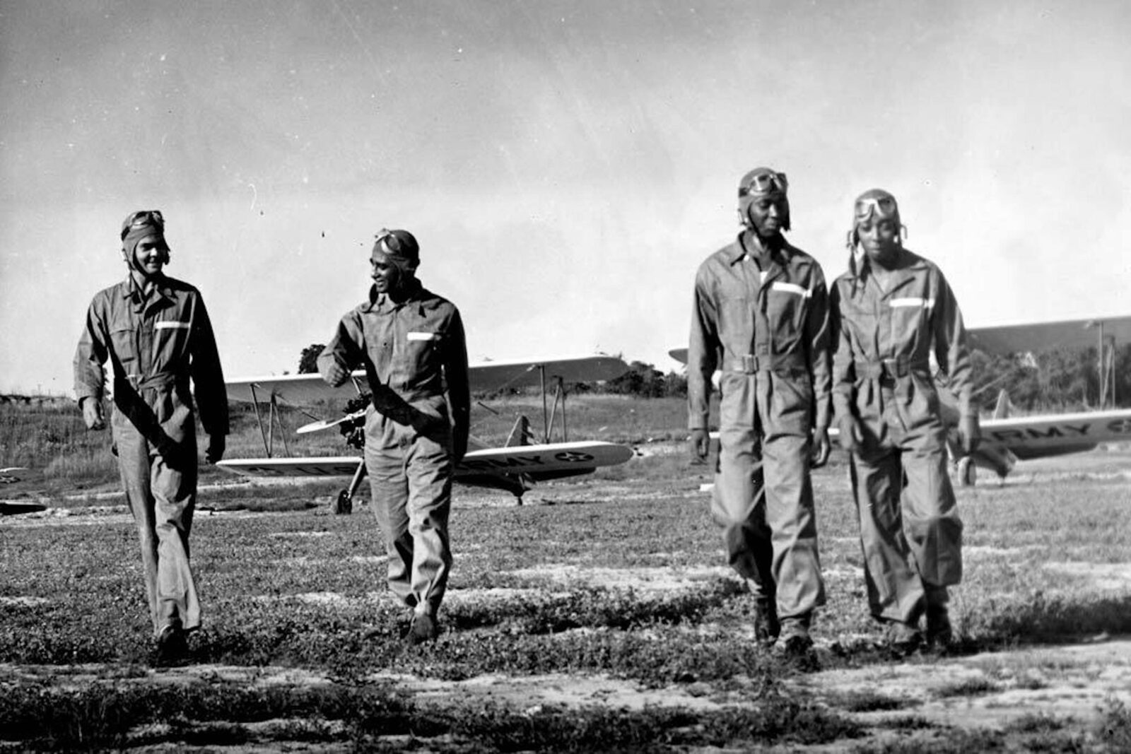 Four black pilots walk away from their planes in a field.