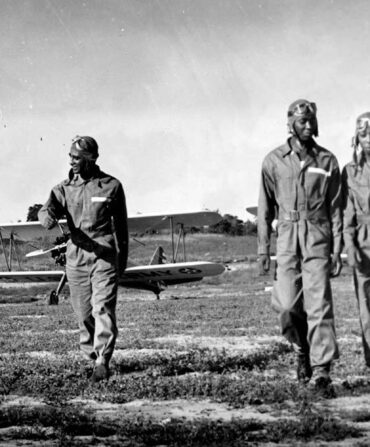 Four black pilots walk away from their planes in a field.