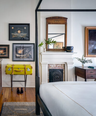 Inside a hotel room with antique art, an ornate old fireplace, and a yellow suitcase