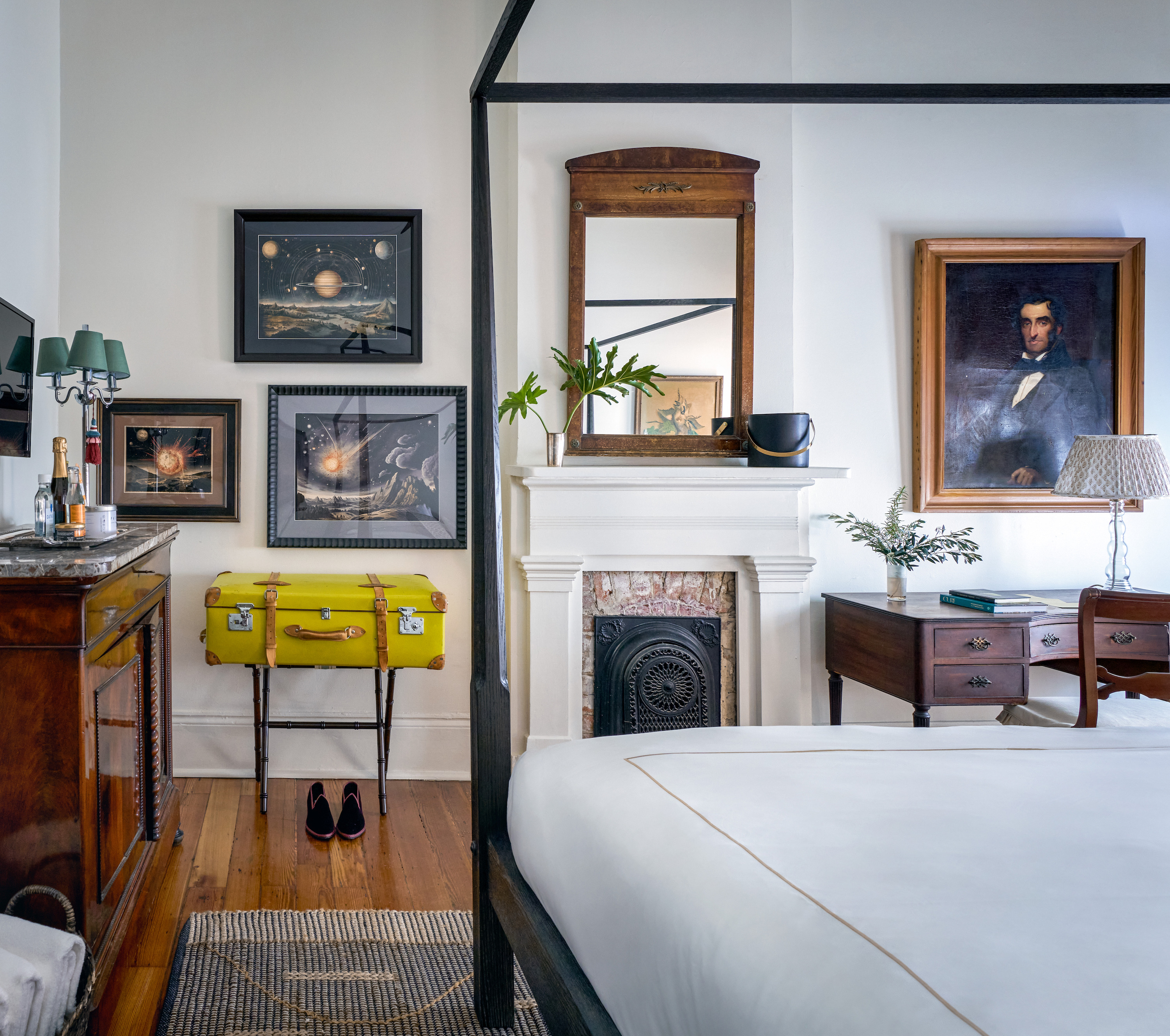 Inside a hotel room with antique art, an ornate old fireplace, and a yellow suitcase