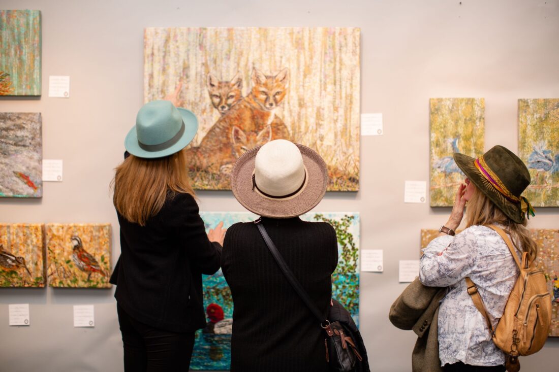 Women looking at sporting art on a wall, including a painting of a fox