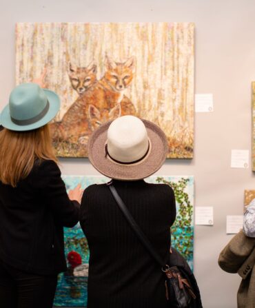 Women looking at sporting art on a wall, including a painting of a fox