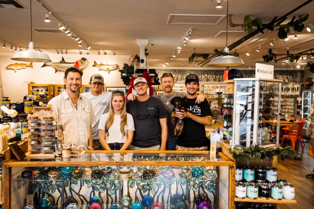 A group of people standing behind the counter in a fly fishing store.