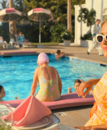 A woman with sunglasses smiles and sits by a pool