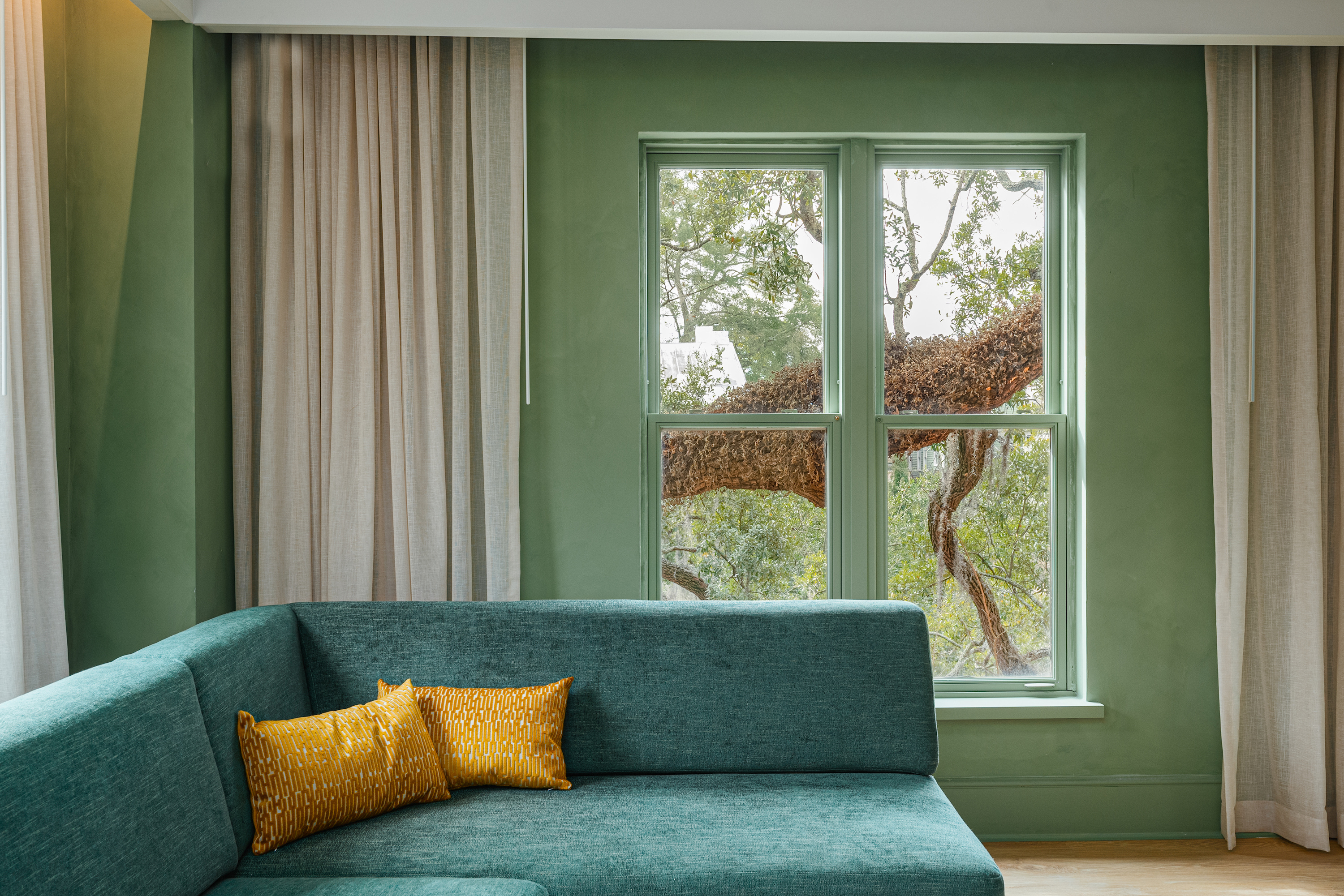 A green suite with a window looking out to branches of an oak tree;