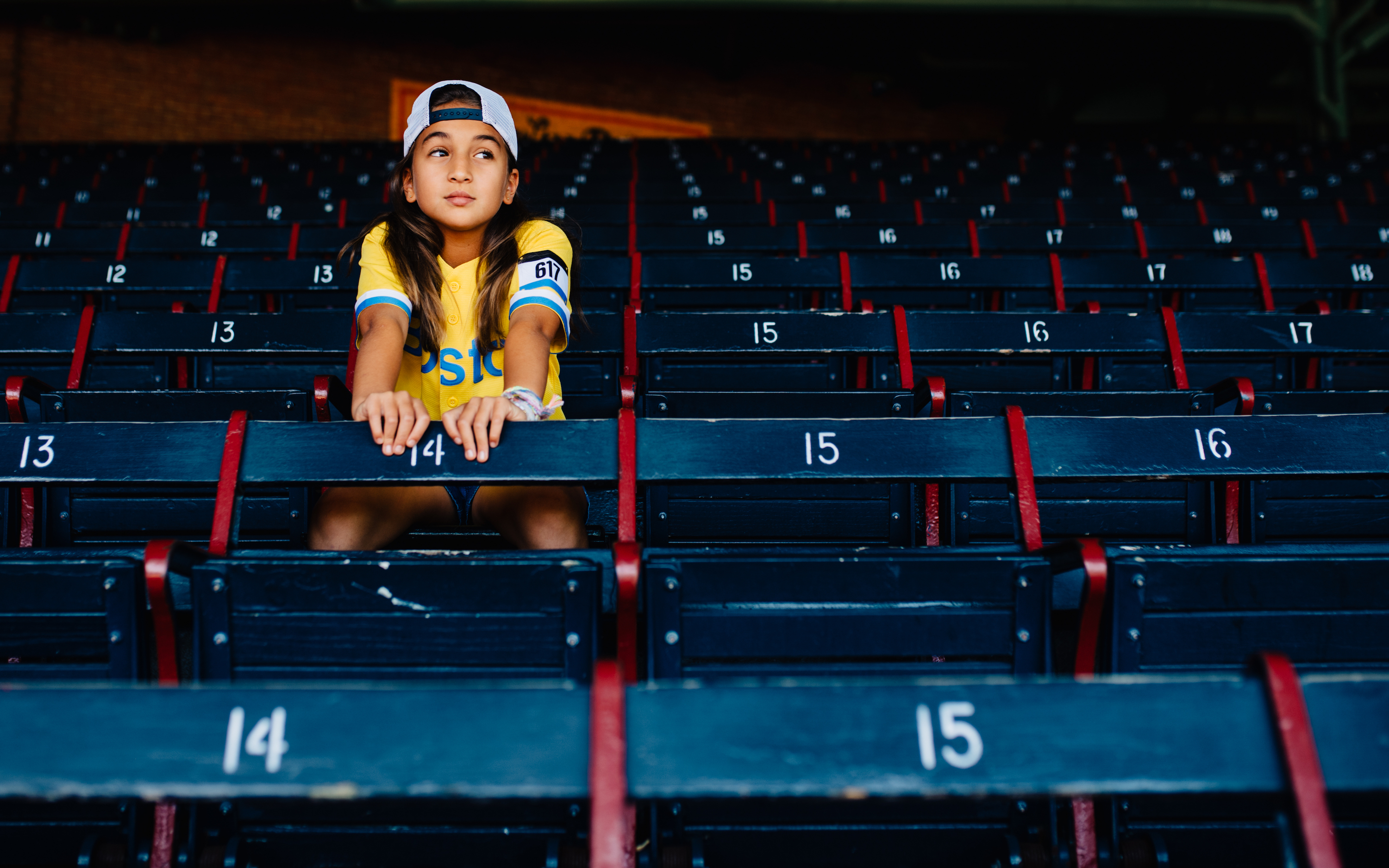 A little girl sits in a stadium with dark blue seats.