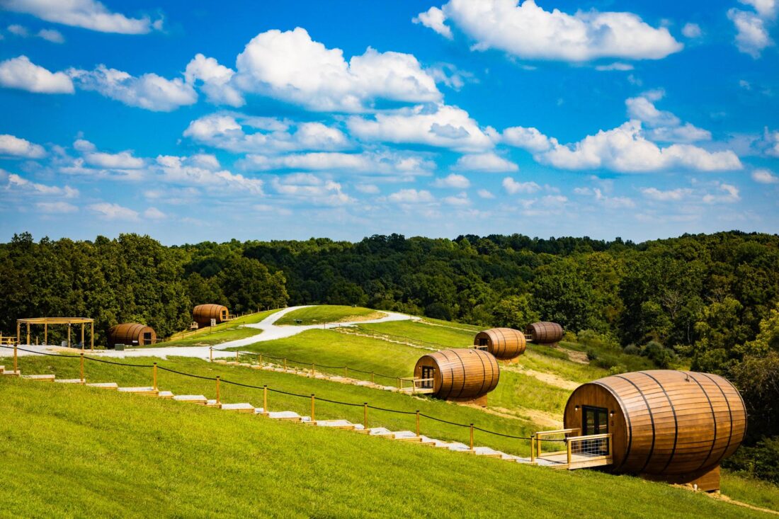 A grassy hill dotted with large bourbon barrel-shaped cabins