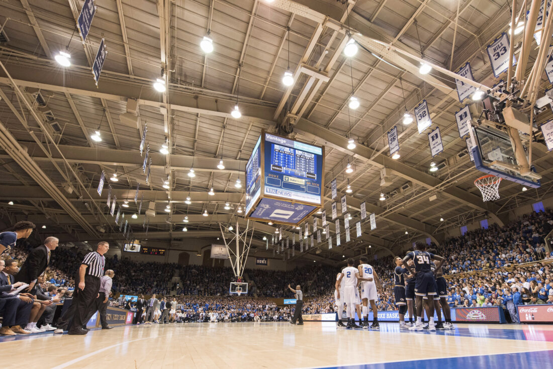 The interior of Duke's Indoor Stadium with two teams huddled up with their coaches on the sidelines.