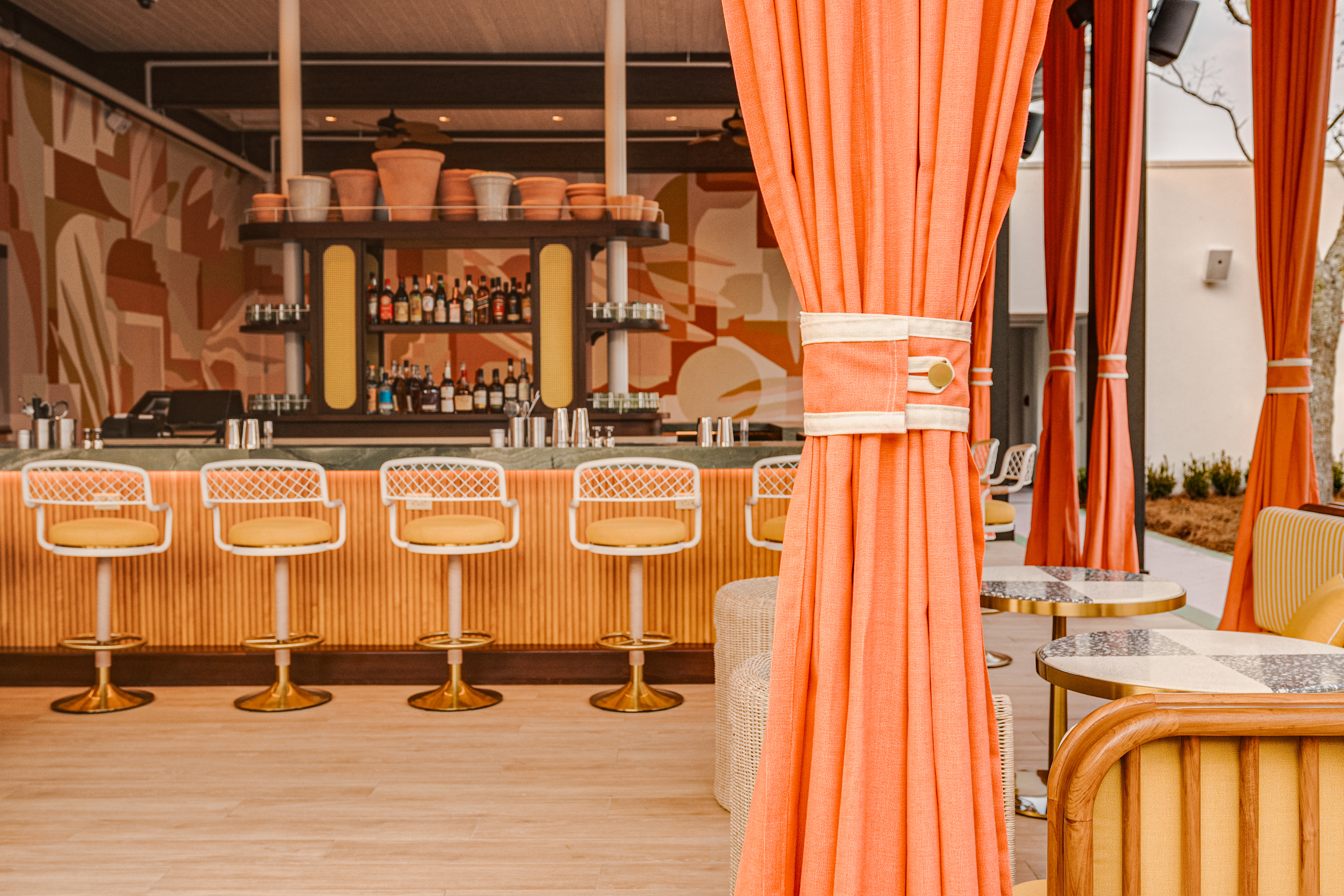 A bright coral and lemon space of an outside bar with curtains and high chairs