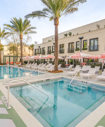 A hotel pool piazza with pink umbrellas, lounge chairs, and striped floor detailing