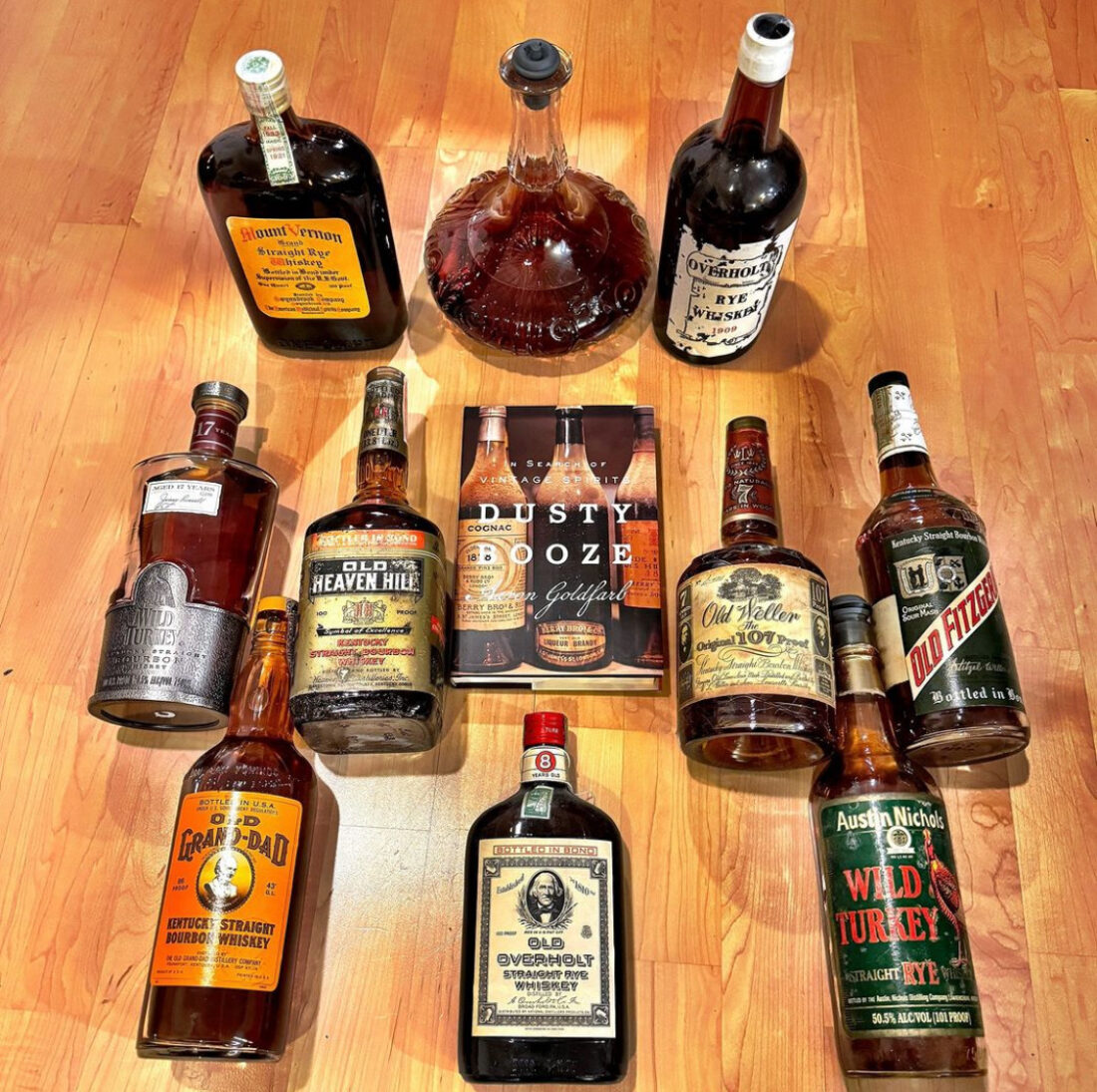 a wood background with 10 bottles of bourbon surrounding a book.