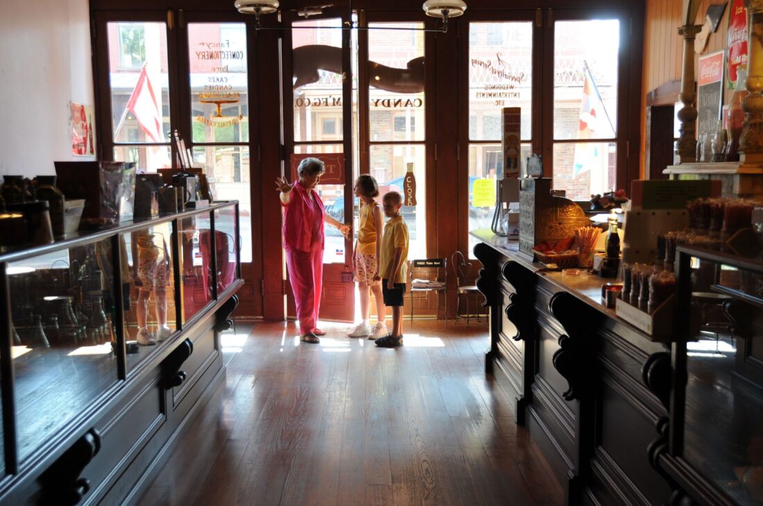 Inside a historic soda shop, a woman shows two children the room