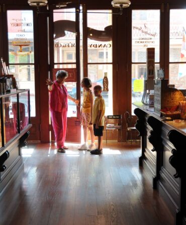 Inside a historic soda shop, a woman shows two children the room