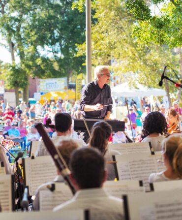 A conductor leading an orchestra on a stage aat a festival
