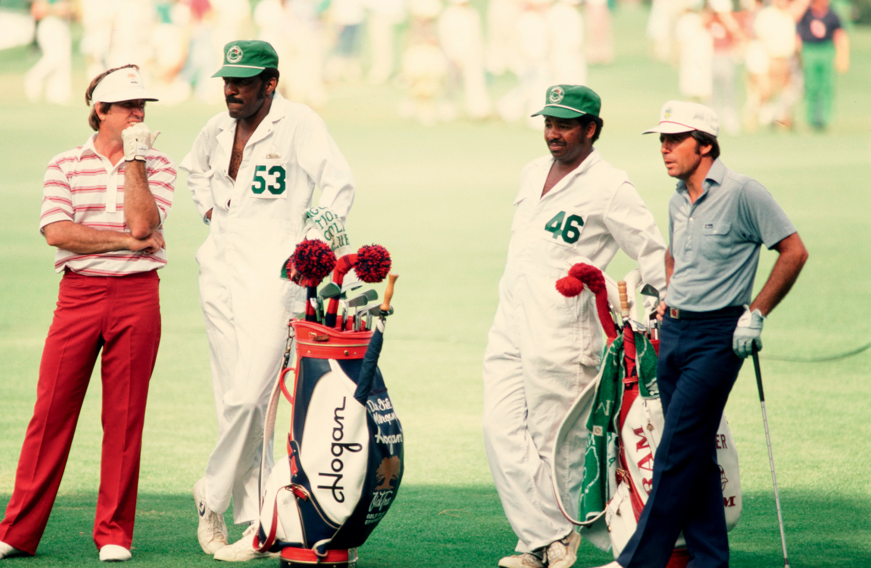 Two caddies and two golfers stand on the green