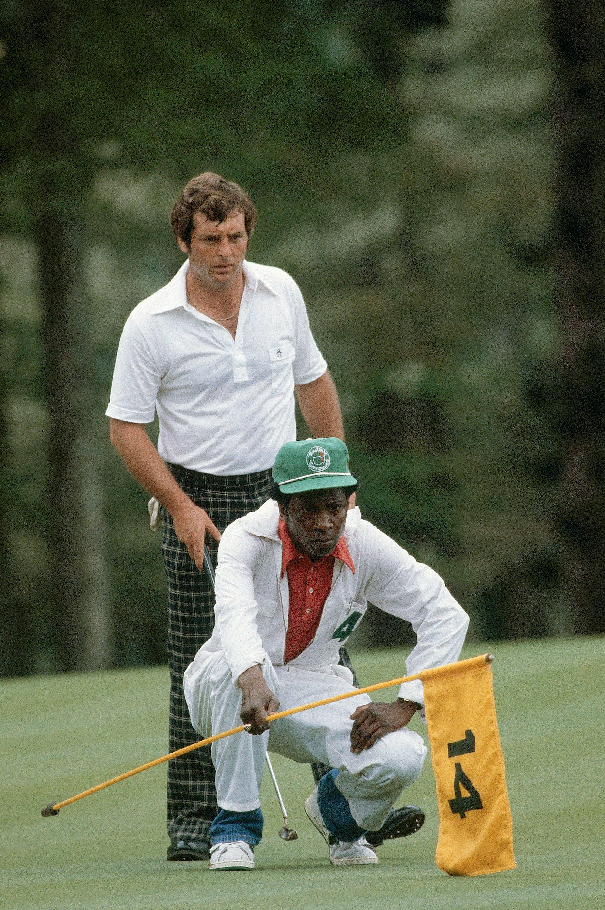 A caddy crouches on the ground with a golfer behind him
