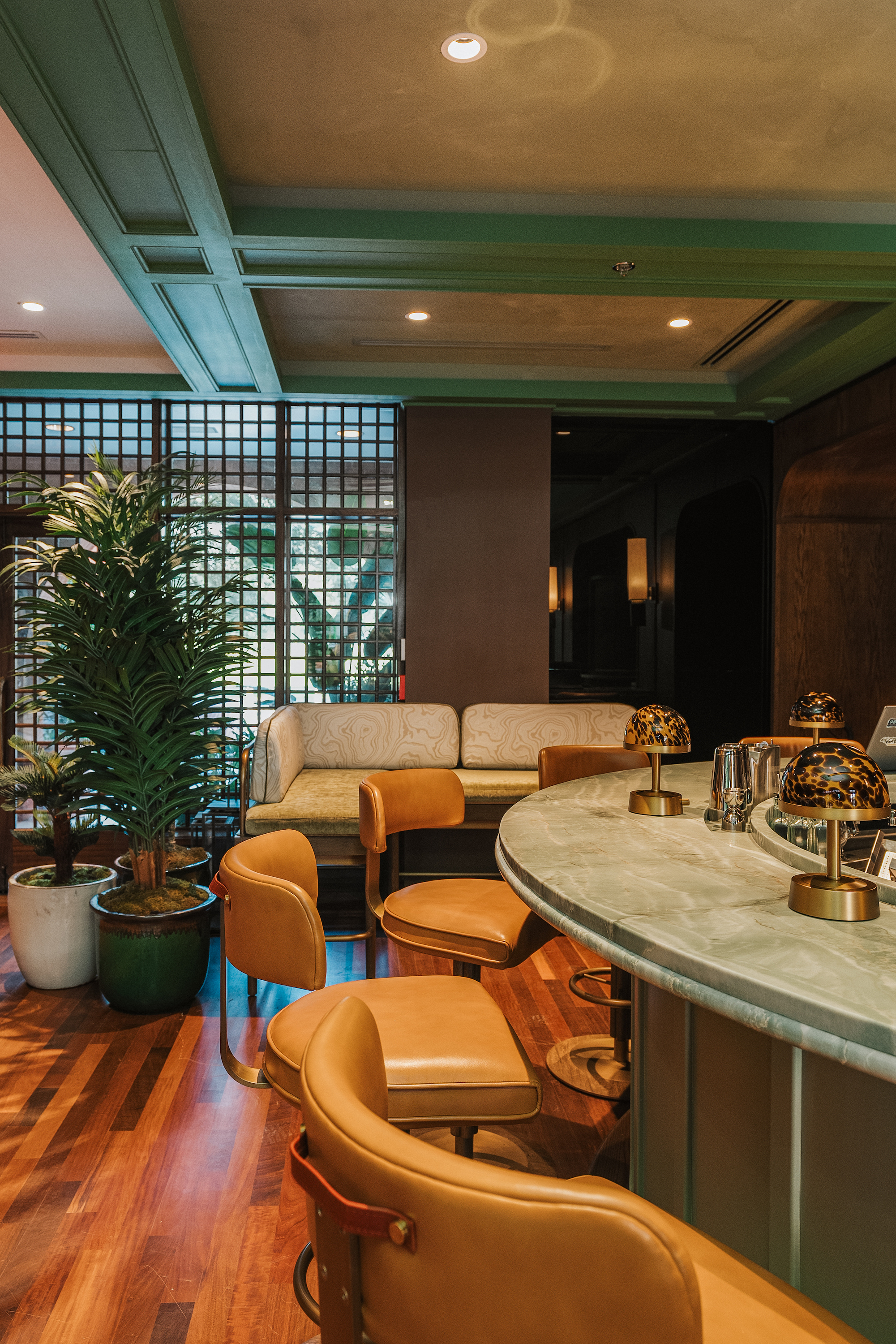 The circle-shaped bar of the Green Room, which nods to midcentury-modern design, is a dimly lit lounge with upholstered banquettes in slate and sage tones and handsome leather bar seats.