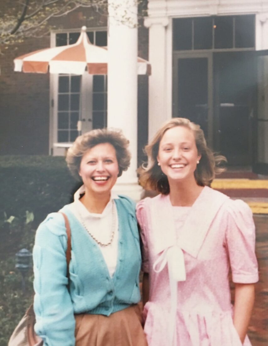 A vintage photo of two women; the one on the left wears a light teal sweater, the one on the right wears a pink dress.