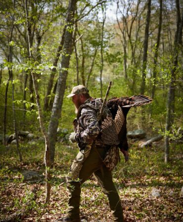A hunter carries a turkey through the woods