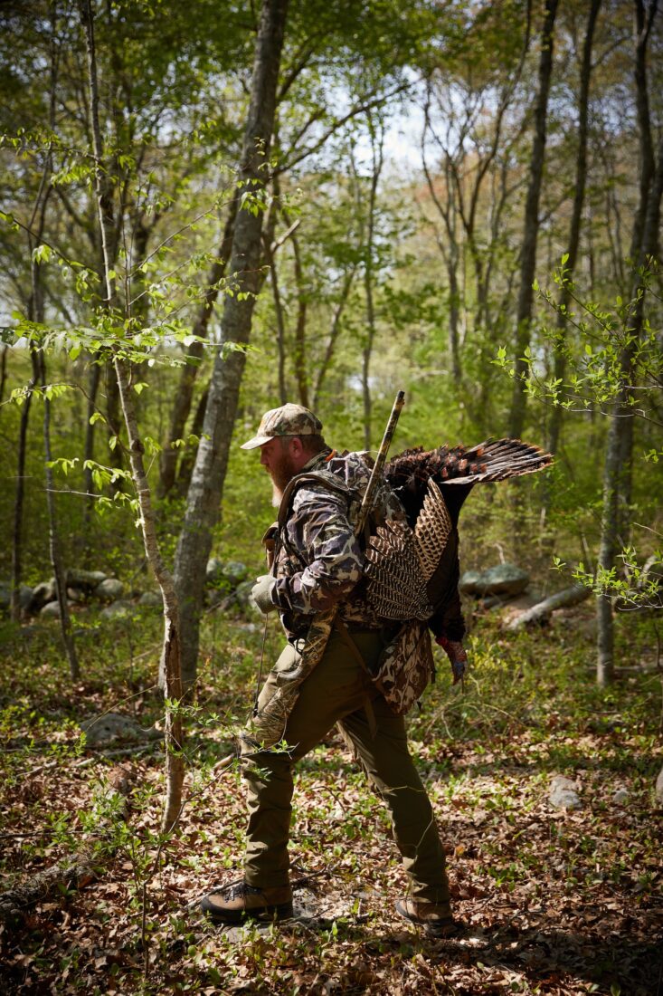 A hunter carries a turkey through the woods