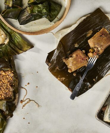 Pasteles De Masa (looks like tamales) rolled into green banana leaves on plates on a white background