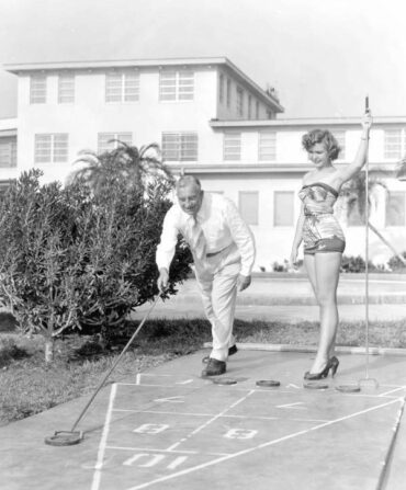 A black and white photo of a man and a woman playing shuffleboard.