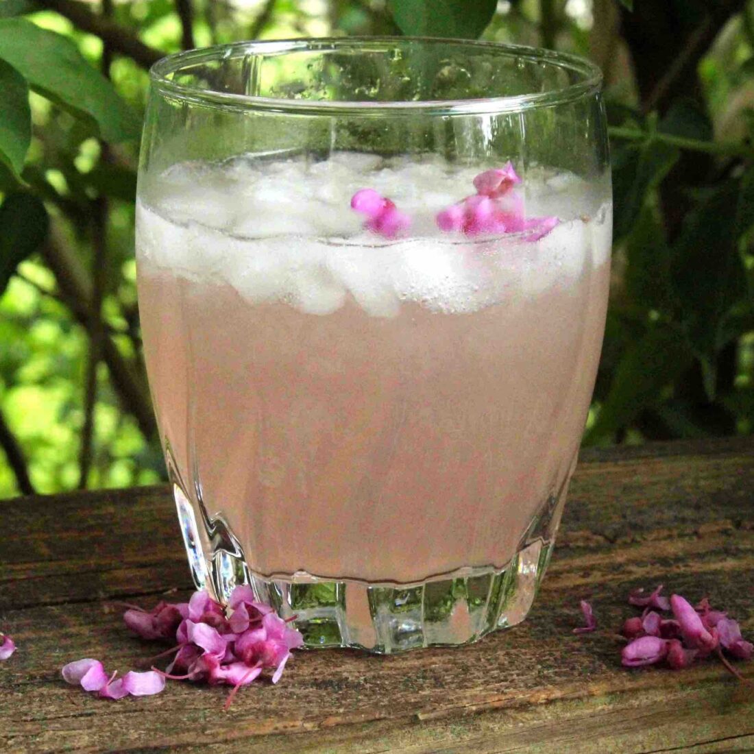 A glass of pink lemonade on a piece of wood outside.