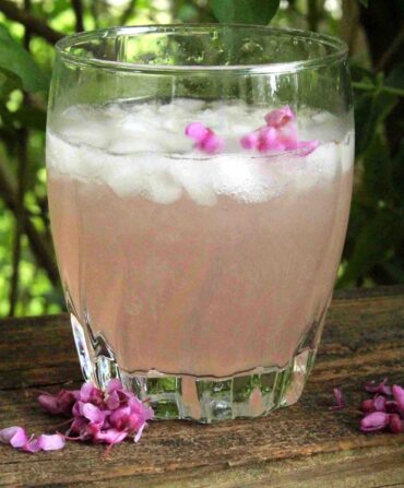 A glass of pink lemonade on a piece of wood outside.
