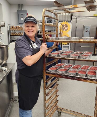 A woman in a kitchen holds a cart with small aluminum tins of meatloaf