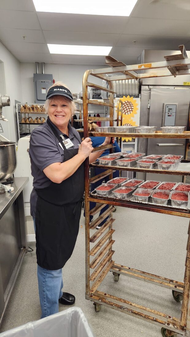 A woman in a kitchen holds a cart with small aluminum tins of meatloaf
