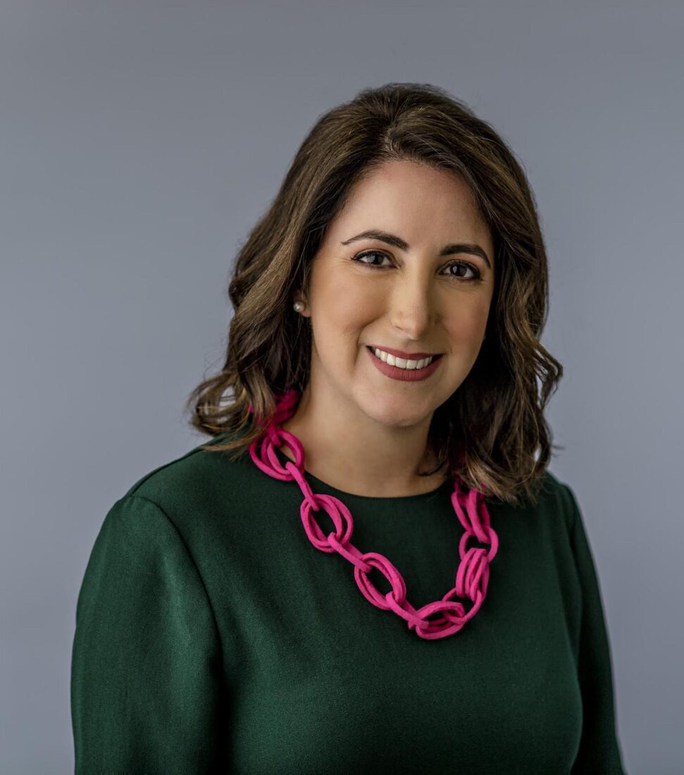 A portrait of a woman in a green top wearing a pink necklace