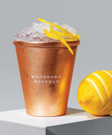 A lemon next to a copper cocktail cup with ice and a lemon peel garnish