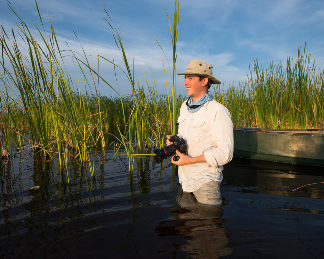 A man stands in a swamp with a camera