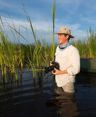 A man stands in a swamp with a camera