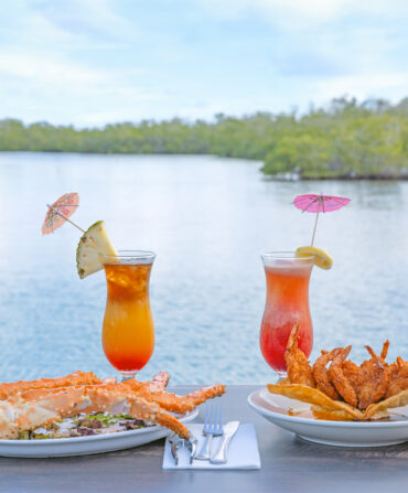 two cocktails and trays of fried seafood on a table overlooking the water