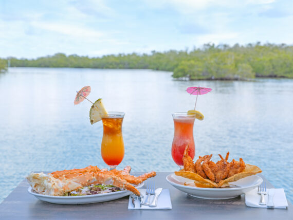 two cocktails and trays of fried seafood on a table overlooking the water