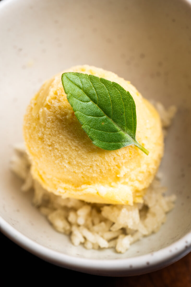 A bowl with yellow ice cream and a mint leaf